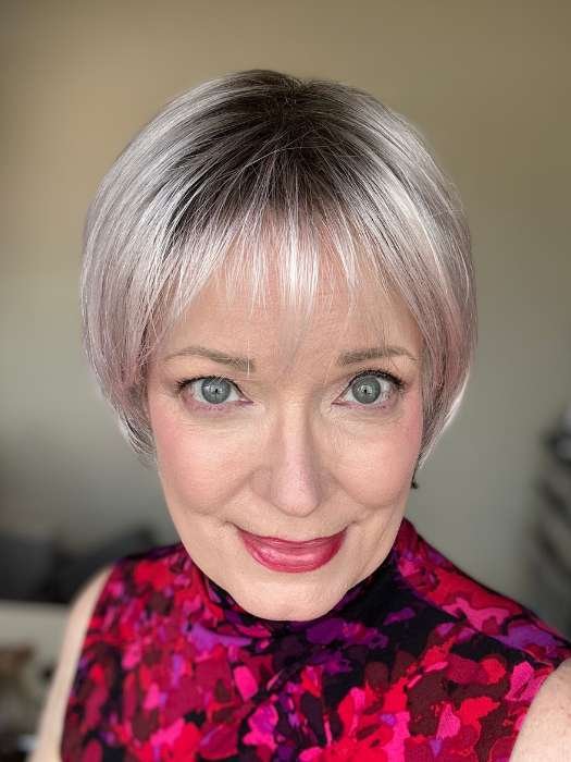 Close up smiling woman wearing a short silver wig for women with soft bangs and subtle pink highlights in natural light