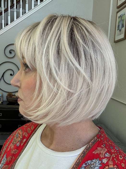 Side view of chin length layered bob in ash blonde with dark roots on model wearing blonde synthetic wig Ellen Wille