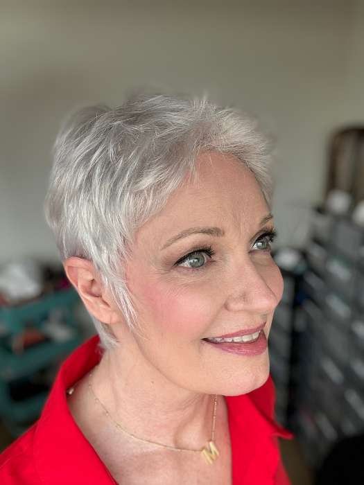 Smiling mature woman wearing short silver pixie with natural hairline, wearing Ellen Wille Risk wig. Red blouse